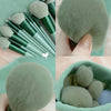 Colección de 13 brochas de maquillaje profesional en tonos verdes y grises para sombra y base.