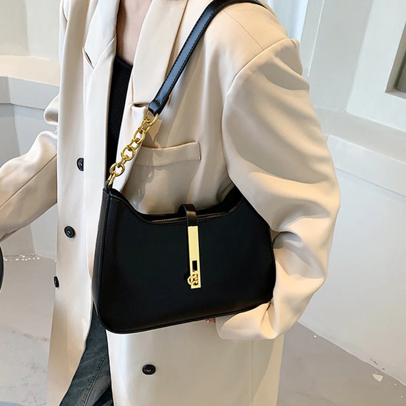 A woman is wearing a black leather hobo shoulder bag with a gold chain strap under a cream blazer.