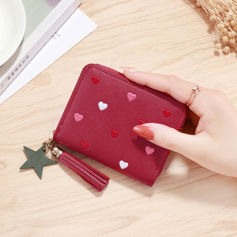 A maroon PU leather wallet with a zipper closure and heart-shaped embellishments is held by a hand on a wooden surface.