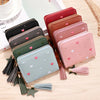 A collection of pink and brown PU leather wallets with tassel closures arranged on a wooden surface.