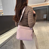 A woman is holding a light pink waterproof nylon crossbody bag with a matching striped sweater in a modern indoor setting.