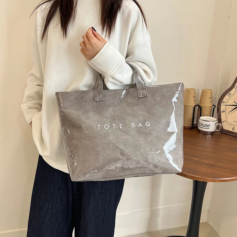 A person holds a gray transparent waterproof PVC tote bag against a light background.