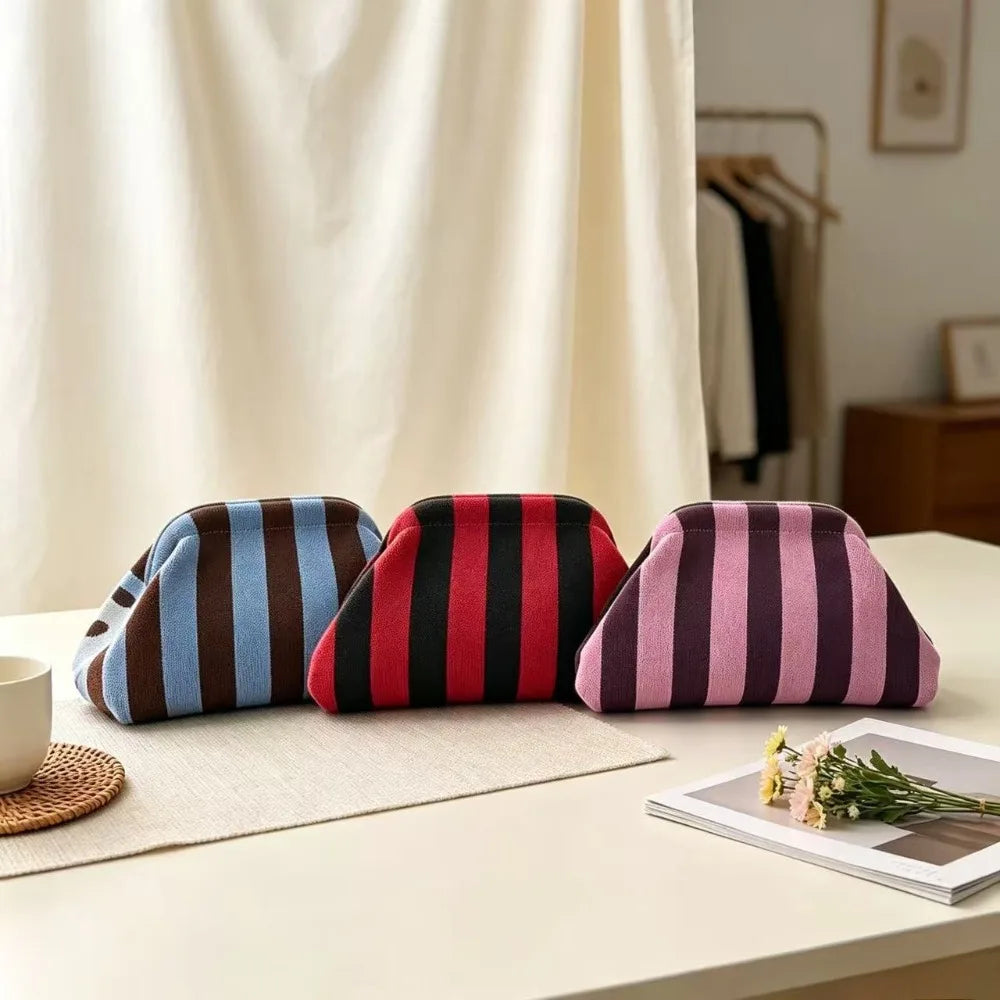 A set of three striped knit cloud makeup bags in navy, maroon, and mauve resting on a light surface.