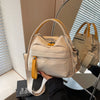 A beige nylon crossbody bag with a top handle is being held by a person against a light background.