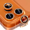 A set of glitter diamond camera lens protectors with metal frames displayed on an orange-colored surface.