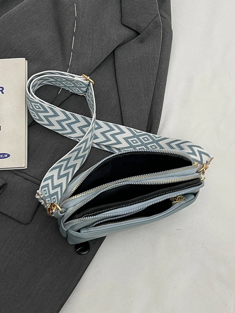 A light blue patterned vegan PU crossbody bag with a gold chain strap resting on a gray blazer.
