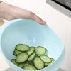 A hand is holding a light blue plastic drain and storage basket filled with sliced cucumbers.