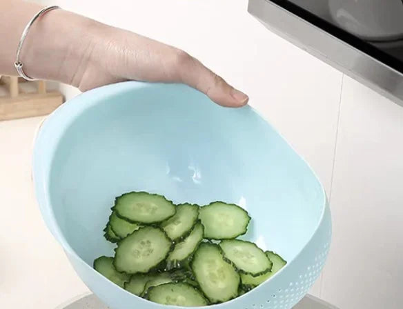 A hand is holding a light blue plastic drain and storage basket filled with sliced cucumbers.
