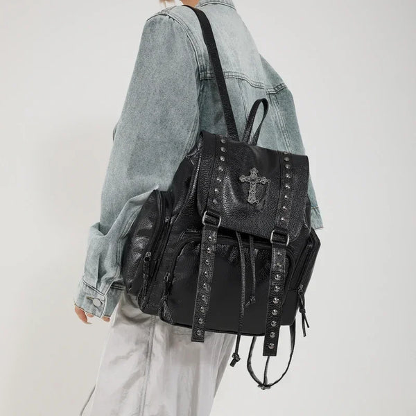 A woman wearing a light denim jacket and white pants carrying a black gothic PU leather riveted backpack.