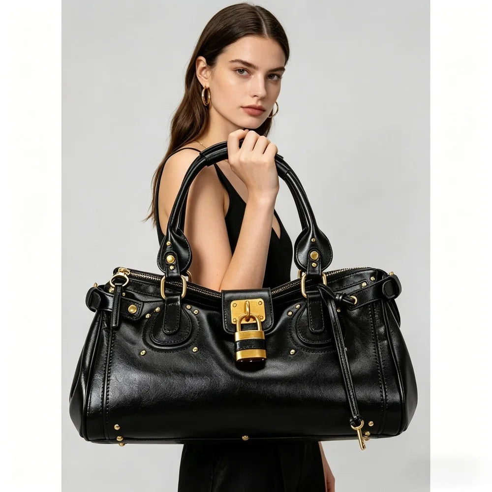 A woman holds a black vegan leather tote bag with gold hardware against a light gray background.