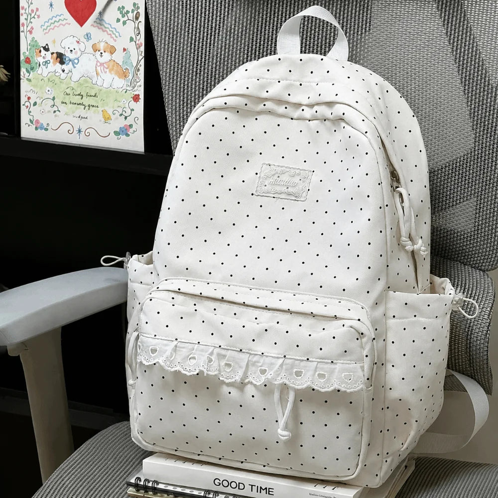 A white polka dot nylon travel backpack with a laptop compartment resting on a gray chair.