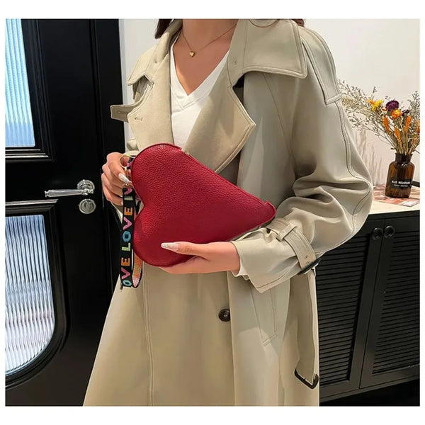 A woman holds a red heart-shaped PU coin purse against a light beige trench coat.