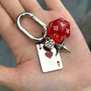 A silver keychain featuring a red dice and a heart-shaped playing card.