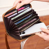 A hand is opening a brown PU leather zipper clutch wallet to show cards and a smartphone inside.