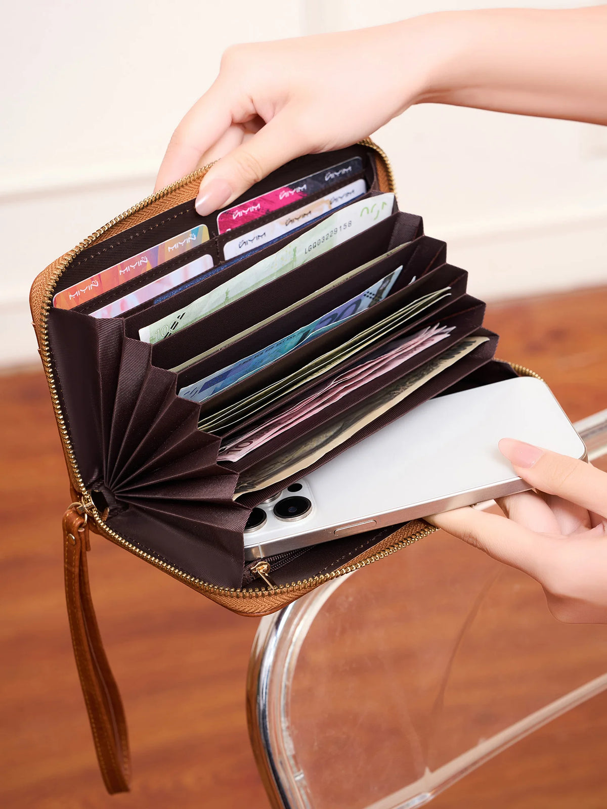 A hand is opening a brown PU leather zipper clutch wallet to show cards and a smartphone inside.