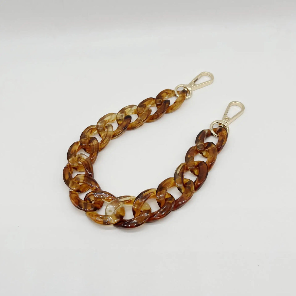 A close-up of a gold-toned, multi-link acrylic chain bracelet with a clasp.