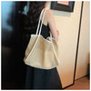 A woman is holding a straw woven tote bag with white trim and a matching pouch against a light-colored wall.