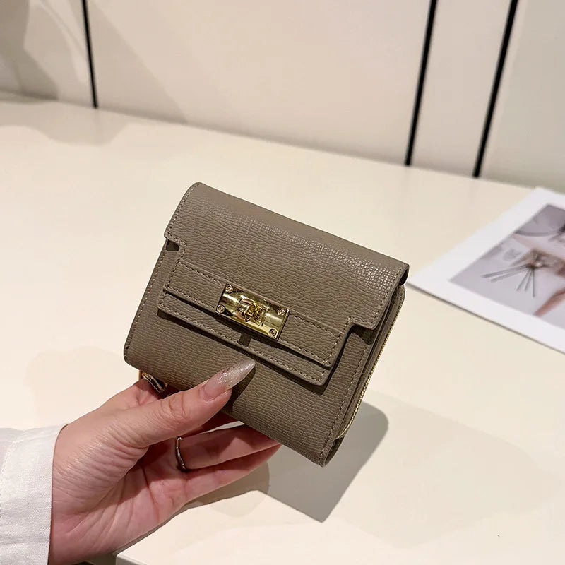 A hand holds a beige multi-slot card holder with gold hardware on a light surface.
