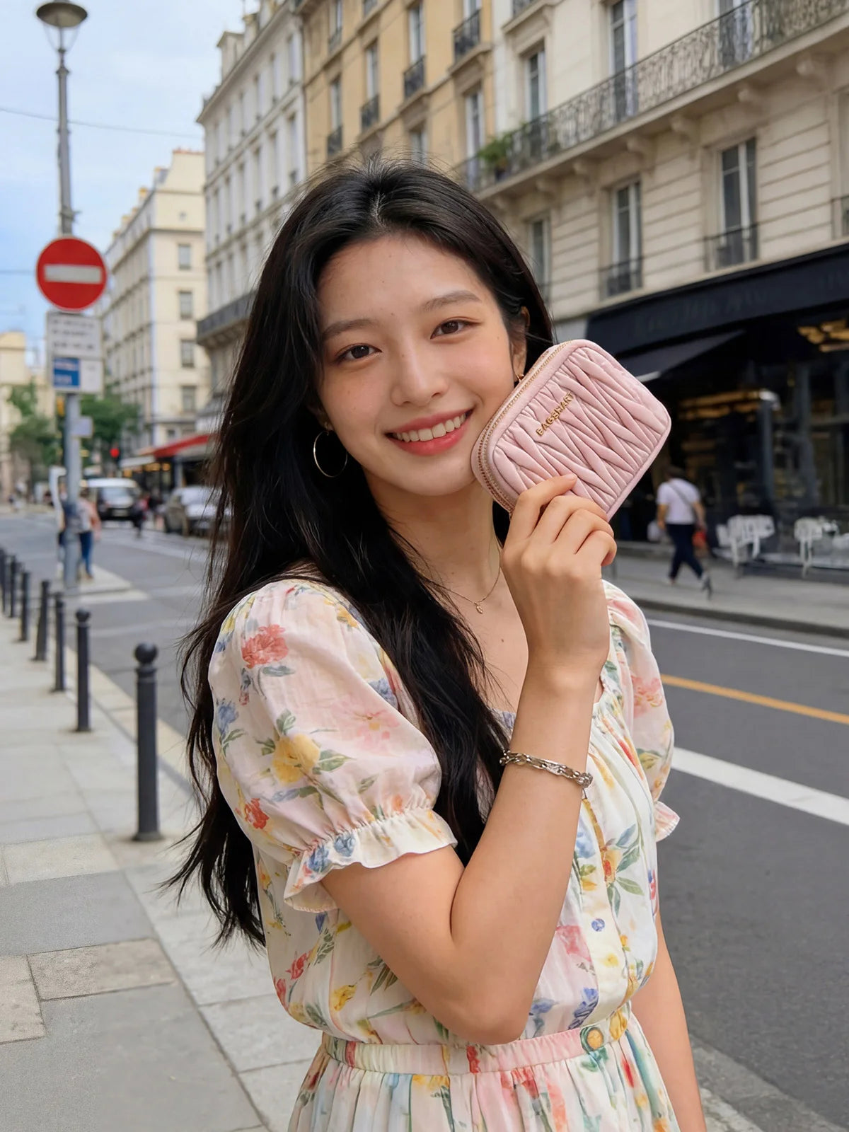 A young woman smiling while holding a pink quilted mini coin purse and card holder wallet outdoors