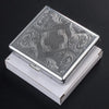 A silver decorative metal cigarette storage box with intricate swirling patterns, resting in its white presentation case.