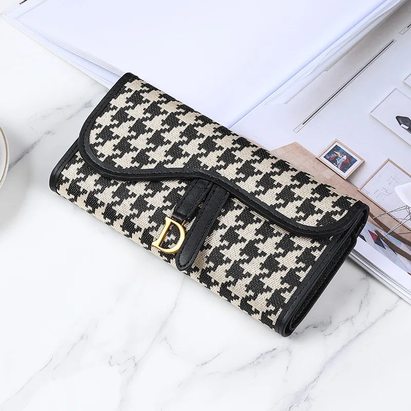 Portefeuille à porte-cartes noir et beige à motif, posé sur une surface en marbre blanc.