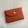 A terracotta-colored genuine leather card holder with a gold-toned clasp resting on a white textured surface.