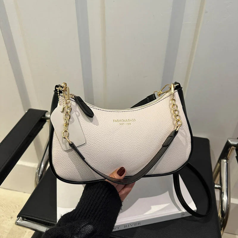 A white leather shoulder bag with gold chain details is displayed on a black surface.