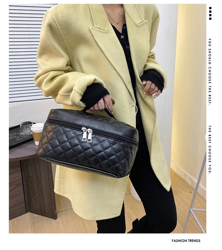 A woman wearing a beige blazer holds a black quilted makeup storage pouch.