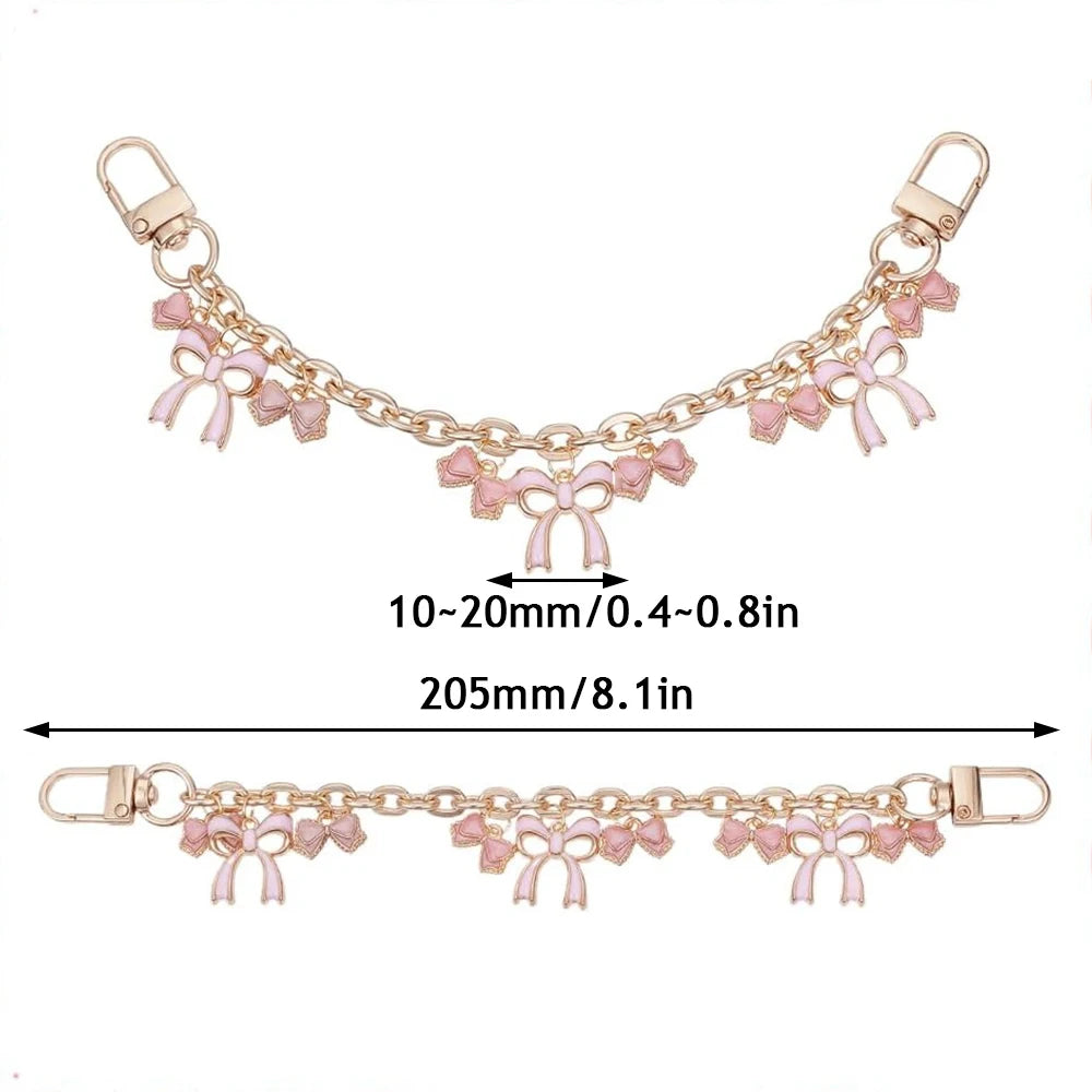 Accesorio de bolso dorado con cadena y detalles de corazón rosa y flor de cerezo.