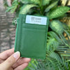 A hand holds a green genuine leather zipper card holder and coin purse with a white tag.