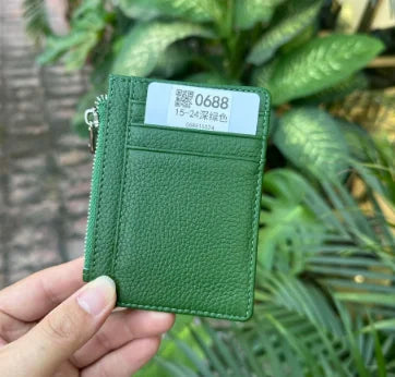 A hand holds a green genuine leather zipper card holder and coin purse with a white tag.