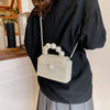 A woman holds a handmade pearl beaded clutch bag with a long pearl strap against a black top.