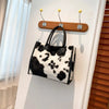 A black and white leopard print faux fur designer shoulder tote bag hanging on a white wall.