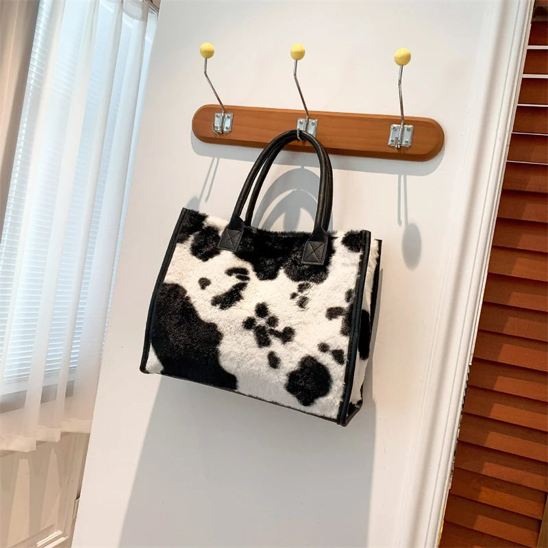A black and white leopard print faux fur designer shoulder tote bag hanging on a white wall.