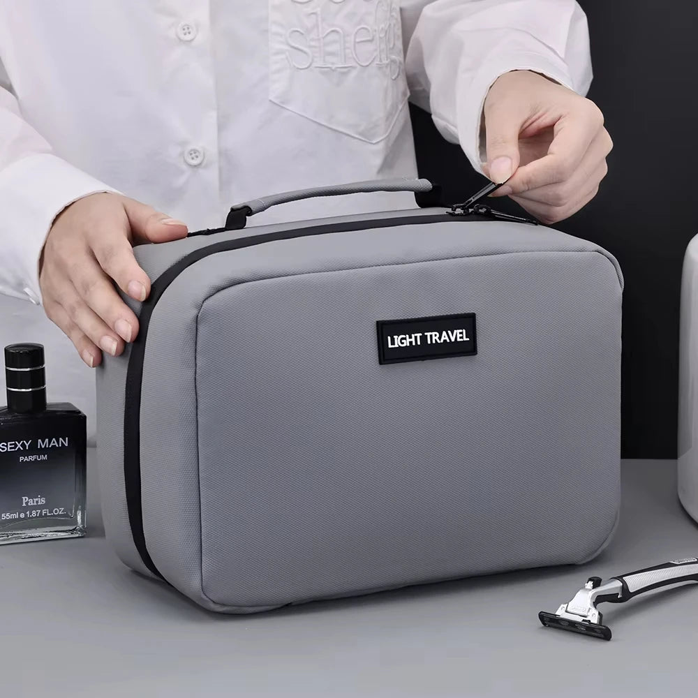 A person holds a gray portable waterproof travel toiletry bag with a black strap and a black label on it.