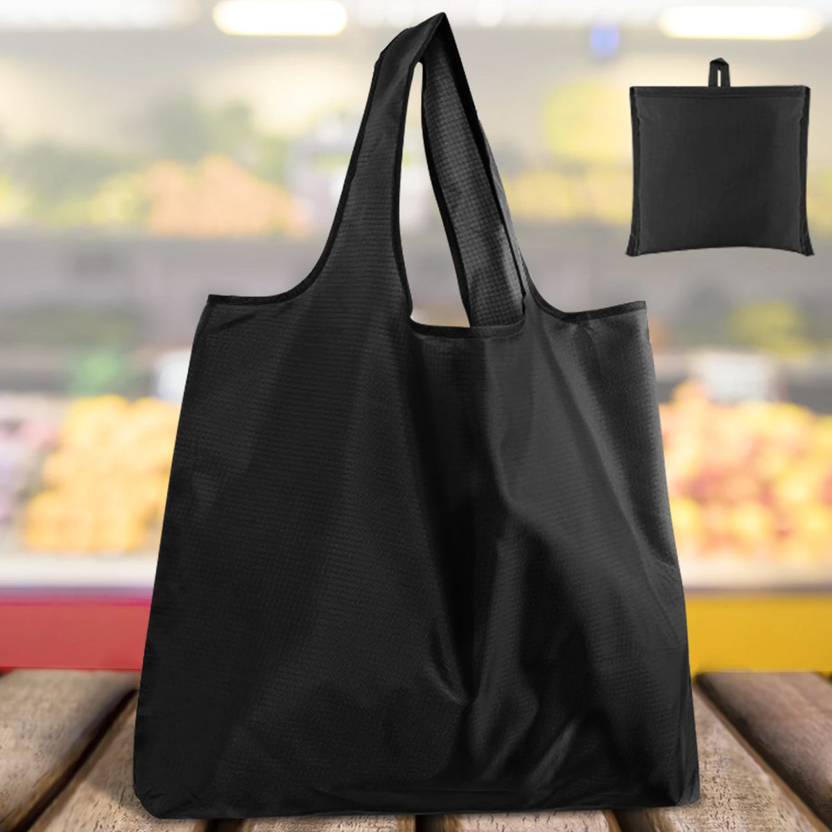 A black reusable foldable grocery tote bag is shown against a blurred background of groceries.