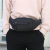 A black canvas waist fanny bag is held by a person wearing a light pink top and black pants.