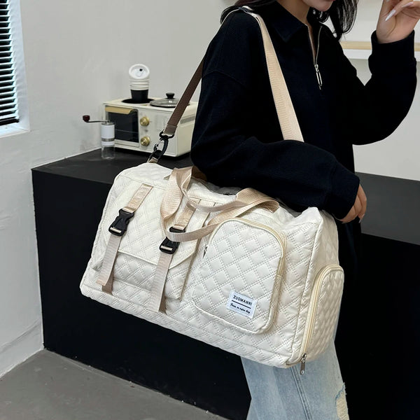 A person holds a cream-colored nylon travel duffle bag with an argyle pattern in a casual indoor setting.