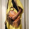 A woman holds a brown fringed clutch bag with tassels against a yellow and black striped garment.