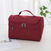 A maroon portable toiletry bag with a handle is shown resting on a white surface next to some papers.