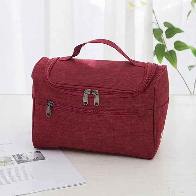 A maroon portable toiletry bag with a handle is shown resting on a white surface next to some papers.