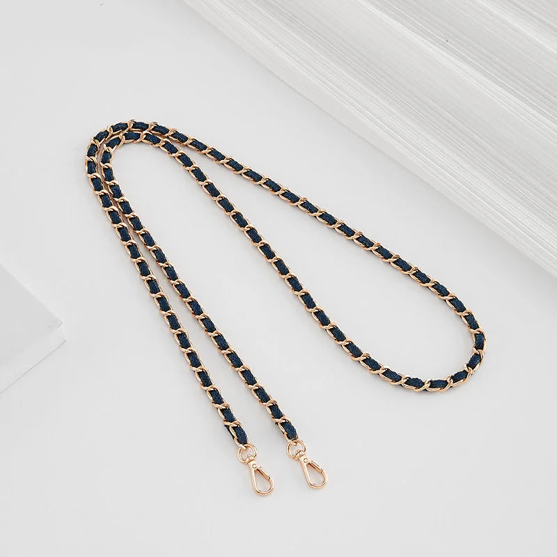 A close-up of a gold-toned leather strap with dark blue stitching and an adjustable buckle.