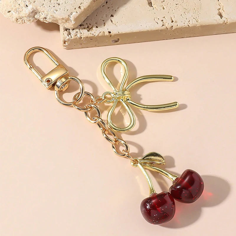 Clé portkey en chaîne dorée avec un charm de nœud et des perles de cerises rouges pendantes.