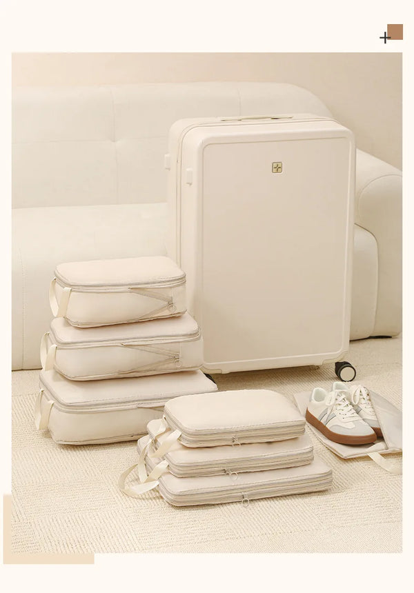 A white 4-piece set of compressible travel storage cubes, including a large suitcase and smaller bags, displayed on a light b
