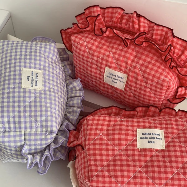A close-up of three quilted makeup pouches in red and white checkered fabric with lace trim.