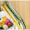 A woven storage basket filled with colorful rolled fabric bundles in yellow, green, pink, and yellow-striped linen.