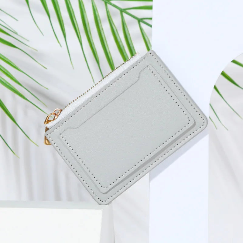A light gray PU leather mini card holder wallet with a zipper and gold hardware is shown against a white background with gree