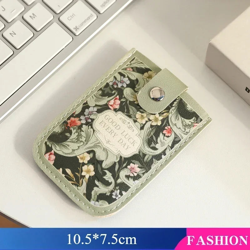 A light green floral patterned PU card wallet with a flap resting on a white desk next to a laptop keyboard.
