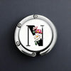 A silver metal fold-over letter hanger hook with a decorative floral design on the surface.