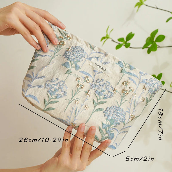 A hand holds a floral canvas makeup bag, showing its size and texture.